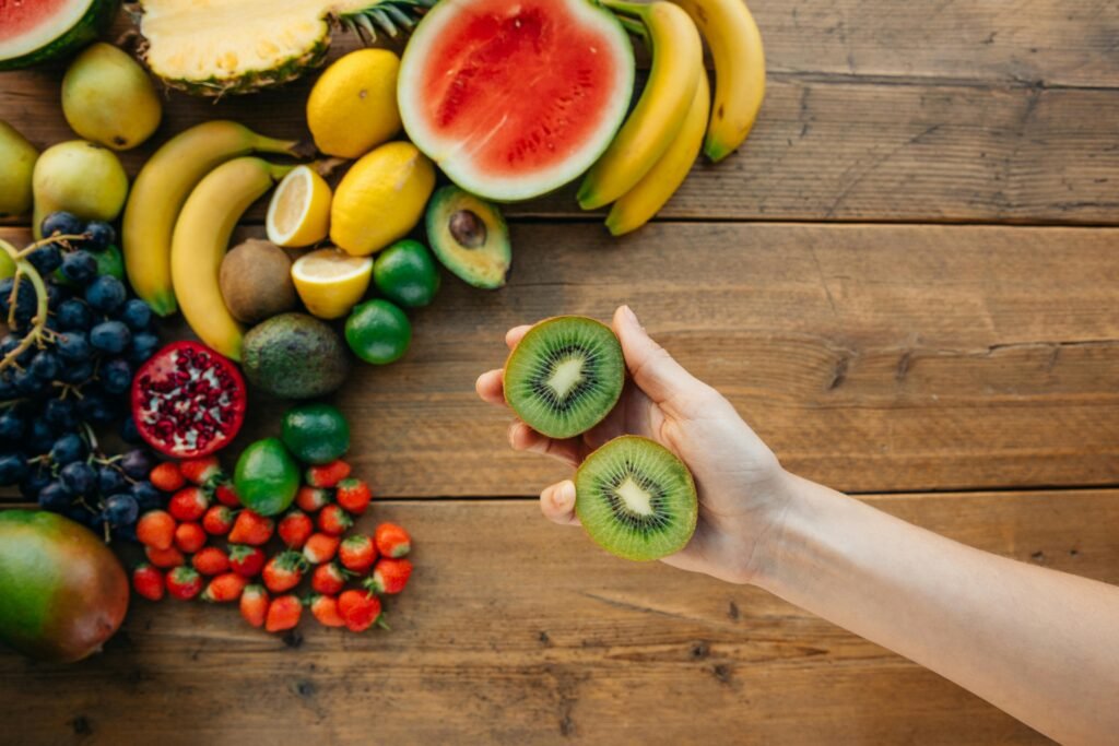 A vibrant assortment of fresh fruits on a wooden table, featuring a hand holding sliced kiwi, perfect for health and lifestyle themes.