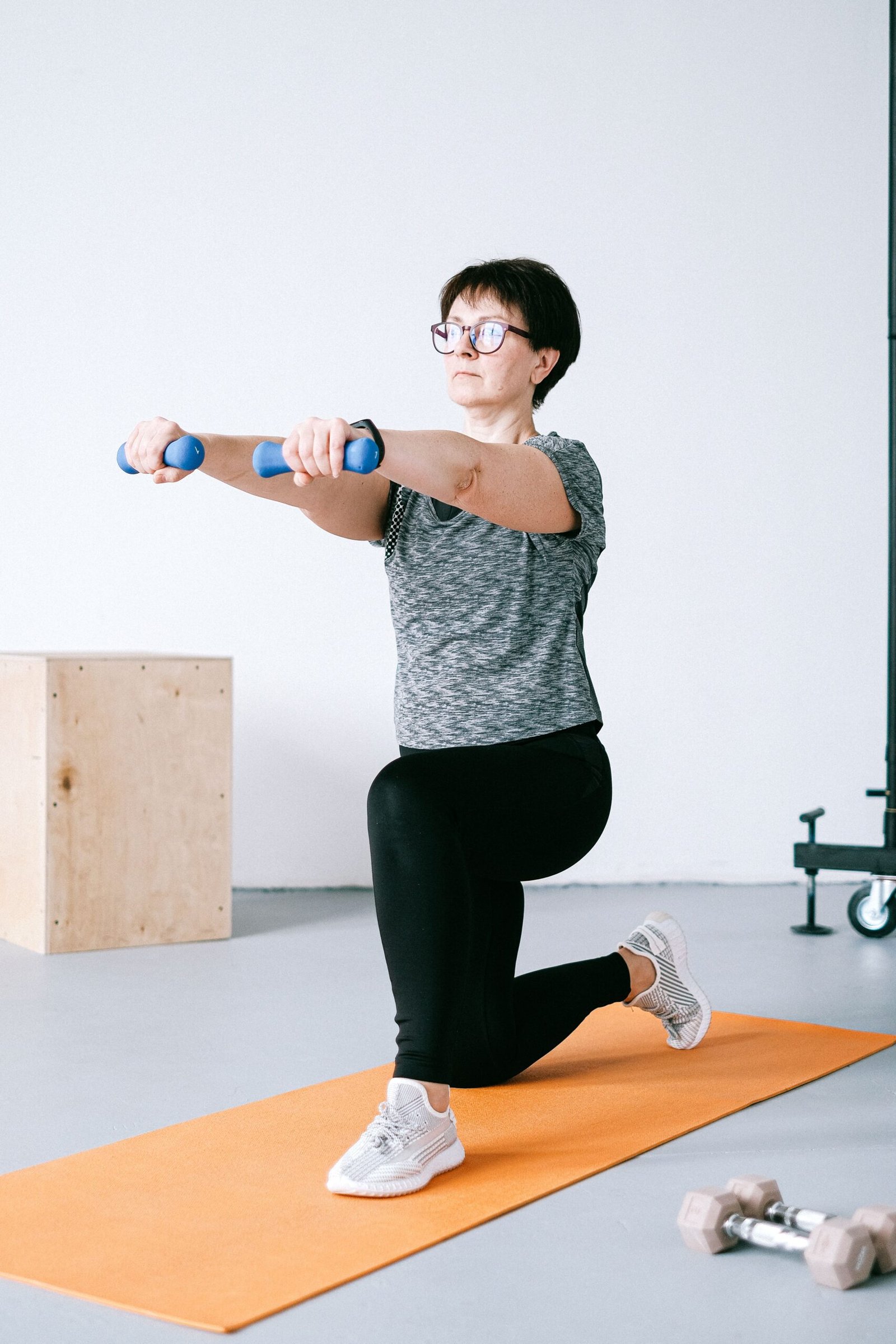 Adult woman exercising indoors with dumbbells on an orange mat for a healthy lifestyle.